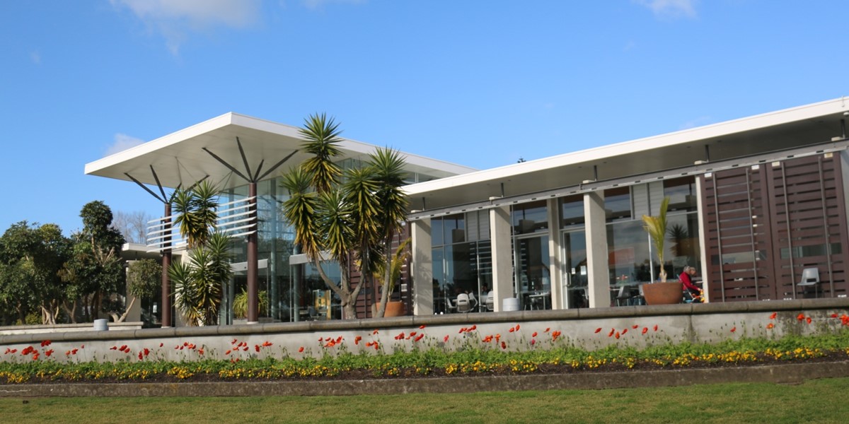 The image shows the visitor centre terrace on a sunny day with chairs and tables under the eaves set up for customers of cafe Miko.  The blooms of red poppies adorn the foreground below the terrace.