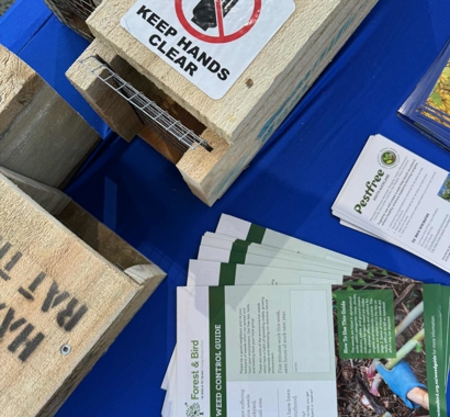  Image shows wooden pest traps with a sticker on top saying 'keep hands clear' alongside some brochures from Forest and Bird.
